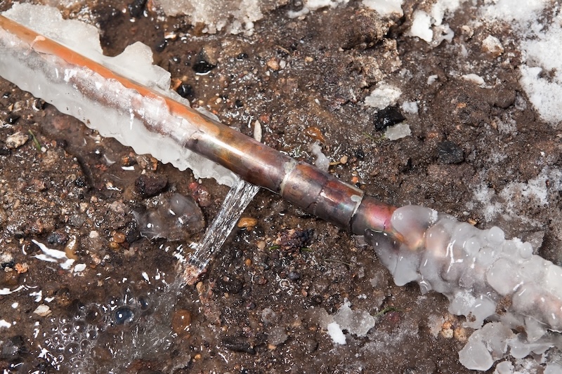 A 3/4" copper water main has frozen and cracked below ground outside a house. This is the line which runs from the street and services and individual house. In extreme cold this pipe can freeze and burst causing costly repairs. The background is excavated dirt.
